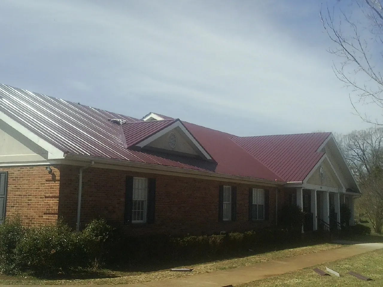 Red metal roof with gabled entries on a long brick building, from a Hail Damage Roof Repair job in Amarillo
