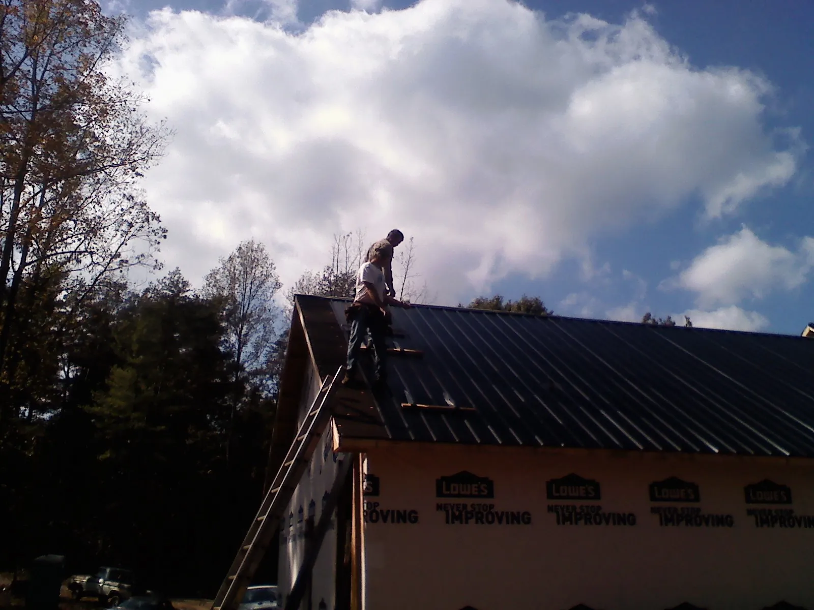 Roofer fastening dark metal panels high against a cloudy sky, from a Roof Inspection job in Amarillo